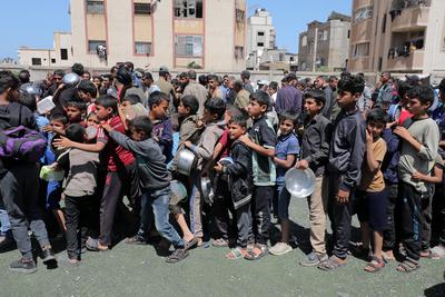 Palestinians, mostly children, wait in long lines with empty pots in hands to get a warm meal distributed by charitable-stock-foto