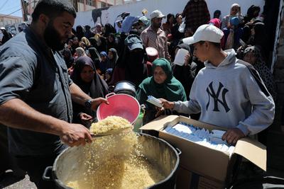 Palestinians, mostly children, wait in long lines with empty pots in hands to get a warm meal distributed by charitable-stock-foto