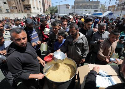Palestinians, mostly children, wait in long lines with empty pots in hands to get a warm meal distributed by charitable-stock-foto
