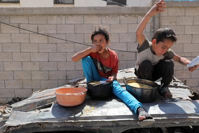 Palestinians, mostly children, wait in long lines with empty pots in hands to get a warm meal distributed by charitable-stock-foto