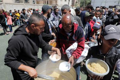 Palestinians, mostly children, wait in long lines with empty pots in hands to get a warm meal distributed by charitable-stock-foto