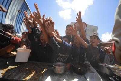 Palestinians, mostly children, wait in long lines with empty pots in hands to get a warm meal distributed by charitable-stock-foto