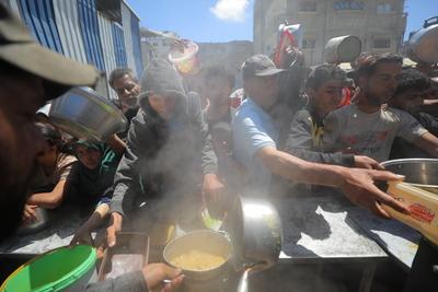 Palestinians, mostly children, wait in long lines with empty pots in hands to get a warm meal distributed by charitable-stock-foto