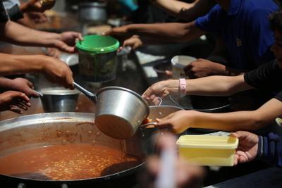 Palestinians, mostly children, wait in long lines with empty pots in hands to get a warm meal distributed by charitable-stock-foto