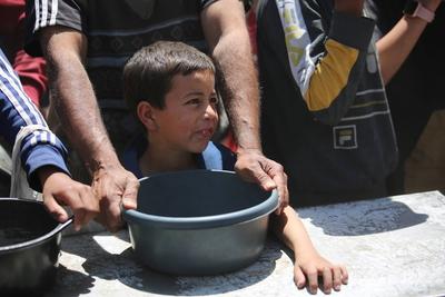 Palestinians, mostly children, wait in long lines with empty pots in hands to get a warm meal distributed by charitable-stock-foto