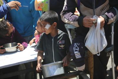 Palestinians, mostly children, wait in long lines with empty pots in hands to get a warm meal distributed by charitable-stock-foto