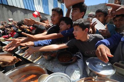 Palestinians, mostly children, wait in long lines with empty pots in hands to get a warm meal distributed by charitable-stock-foto