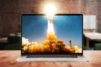 Concept Gl?hbirne leuchtet und hebt erfolgreich mit Rauch und Wolken vom Laptop-Display auf h?lzernem Desktop im B?ro ab-stock-photo