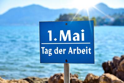 Germany - April 18, 2025: PHOTOMONTAGE, Labor Day, May 1 holiday, lettering on a sign in nature in front of the sea in t-stock-foto