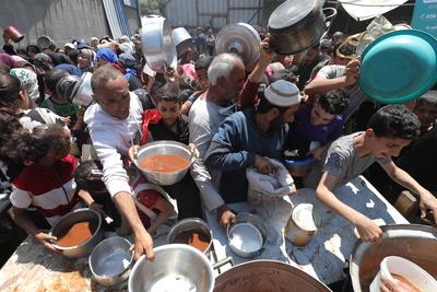 Palestinians wait in long queues to receive pots of food distributed by charitable organizations-stock-photo