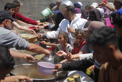 Palestinians wait in long queues to receive pots of food distributed by charitable organizations-stock-photo