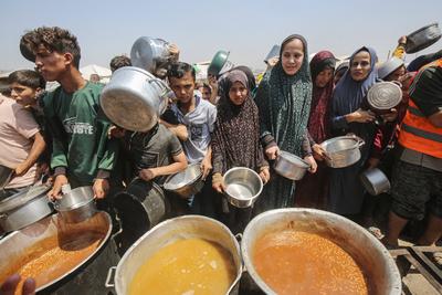 Palestinians wait in long queues to receive pots of food distributed by charitable organizations, in Gaza city-stock-photo