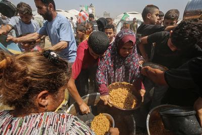 Palestinians wait in long queues to receive pots of food distributed by charitable organizations, in Gaza city-stock-foto