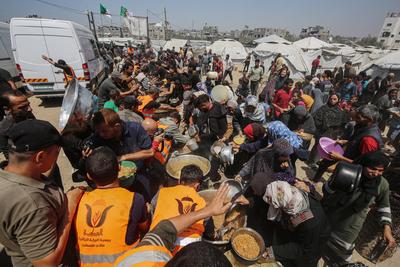Palestinians wait in long queues to receive pots of food distributed by charitable organizations, in Gaza city-stock-foto