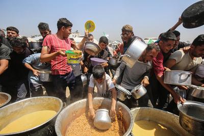 Palestinians wait in long queues to receive pots of food distributed by charitable organizations, in Gaza city-stock-foto