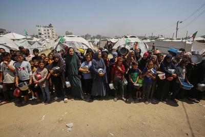 Palestinians wait in long queues to receive pots of food distributed by charitable organizations, in Gaza city-stock-foto