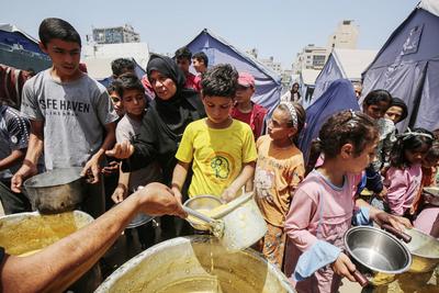 Palestinians wait in long queues to receive pots of food distributed by charitable organizations, in Gaza city-stock-foto