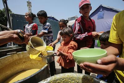 Palestinians wait in long queues to receive pots of food distributed by charitable organizations, in Gaza city-stock-foto
