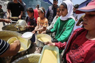 Palestinians wait in long queues to receive pots of food distributed by charitable organizations, in Gaza city-stock-foto
