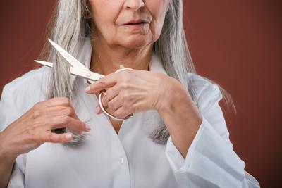 Portrait of unhappy senior woman cutting her hair because of cancer. Breast cancer awareness concept. Portrait of unhapp-stock-photo