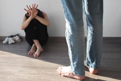 M?dchen, 7-8 Jahre alt, sitzt ver?ngstigt auf dem Boden und bedeckt ihr Gesicht mit den H?nden, vor ihr steht ein w?tender Mann, dessen Gesicht nicht zu sehen ist, Vater oder Stiefvater, Vorstellung von Gewalt, Bestrafung von Kindern-stock-foto