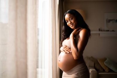 Frau steht vor einem Fenster mit einem Babybauch-stock-foto
