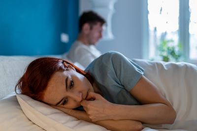 Upset wife lies with her back to husband. Man with disinterested look ignores sad depressed woman. Upset wife lies with-stock-photo