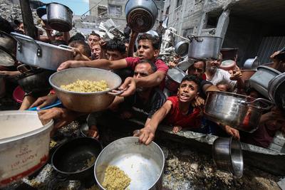 Palestinians wait in long queues to receive pots of food distributed by charitable organizations, in Jabalia-stock-foto