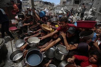 Palestinians wait in long queues to receive pots of food distributed by charitable organizations, in Jabalia-stock-foto