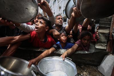 Palestinians wait in long queues to receive pots of food distributed by charitable organizations, in Jabalia-stock-foto