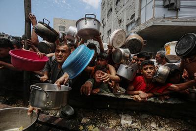 Palestinians wait in long queues to receive pots of food distributed by charitable organizations, in Jabalia-stock-foto