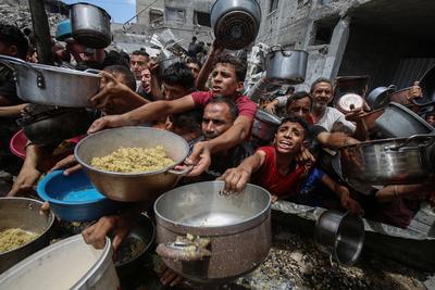 Palestinians wait in long queues to receive pots of food distributed by charitable organizations, in Jabalia-stock-foto