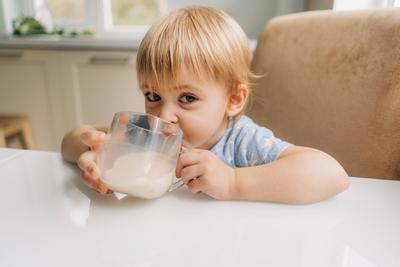 Little toddler girl drinks delicious fresh milk from a mug in the kitchen at home.-stock-photo