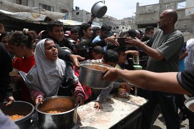 Palestinians who were able to receive the food distributed are eating as Palestinians, including children, who are struggling with hunger wait in line to receive hot meals distributed by the charity organizations-stock-foto