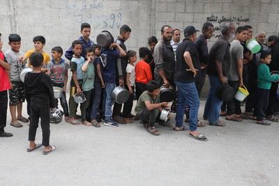 Palestinians who were able to receive the food distributed are eating as Palestinians, including children, who are struggling with hunger wait in line to receive hot meals distributed by the charity organizations-stock-foto