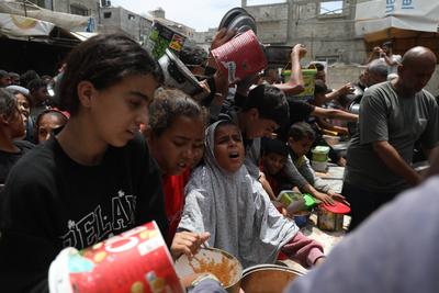 Palestinians who were able to receive the food distributed are eating as Palestinians, including children, who are struggling with hunger wait in line to receive hot meals distributed by the charity organizations-stock-foto