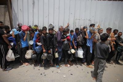 Palestinians who were able to receive the food distributed are eating as Palestinians, including children, who are struggling with hunger wait in line to receive hot meals distributed by the charity organizations-stock-foto