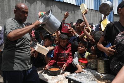 Palestinians who were able to receive the food distributed are eating as Palestinians, including children, who are struggling with hunger wait in line to receive hot meals distributed by the charity organizations-stock-foto