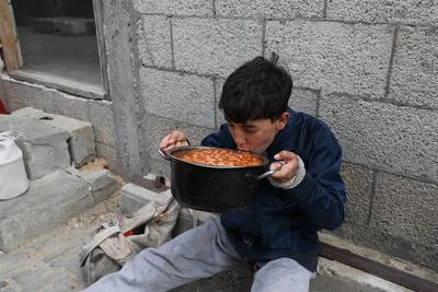 Palestinians who were able to receive the food distributed are eating as Palestinians, including children, who are struggling with hunger wait in line to receive hot meals distributed by the charity organizations-stock-foto
