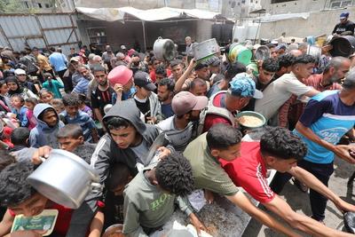 Palestinians who were able to receive the food distributed are eating as Palestinians, including children, who are struggling with hunger wait in line to receive hot meals distributed by the charity organizations-stock-foto