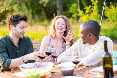 A group of friends having a wonderful time enjoying a picnic outdoors with wine on a sunny day Three friends sharing a j-stock-foto