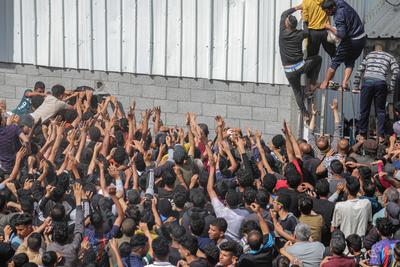 Displaced Palestinians reach out for bread being distributed through a bakery window in Nusseirat Refugee Camp after limited flour supplies entered the Gaza Strip-stock-foto