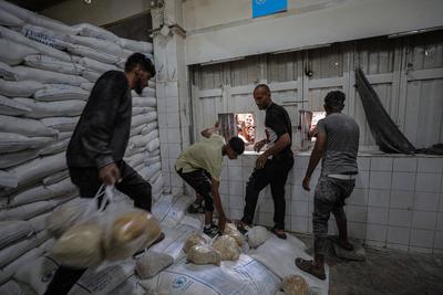 Displaced Palestinians reach out for bread being distributed through a bakery window in Nusseirat Refugee Camp after limited flour supplies entered the Gaza Strip-stock-foto
