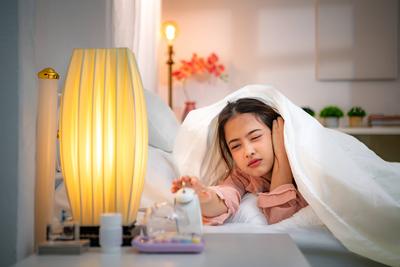 Asian young woman on the bed in the bedroom trying to wake up and prepare for work Asian young woman on the bed in the b-stock-photo