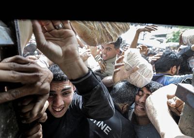 Displaced Palestinians reach out for bread being distributed through a bakery window in Nusseirat Refugee Camp after limited flour supplies entered the Gaza Strip-stock-foto