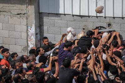Displaced Palestinians reach out for bread being distributed through a bakery window in Nusseirat Refugee Camp after limited flour supplies entered the Gaza Strip-stock-foto