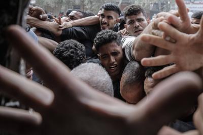 Displaced Palestinians reach out for bread being distributed through a bakery window in Nusseirat Refugee Camp after limited flour supplies entered the Gaza Strip-stock-foto