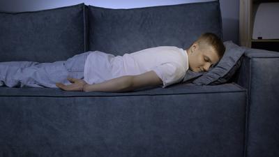 M?der Junge, der sich lustlos auf die Couch legt. Medien. Er f?hlt sich deprimiert, unmotiviert, traurig, gelangweilt. Ersch?pft bricht er vor Stress auf der Couch zusammen.-stock-photo