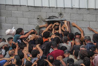 Displaced Palestinians reach out for bread being distributed through a bakery window in Nusseirat Refugee Camp after limited flour supplies entered the Gaza Strip-stock-foto