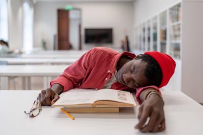 M?der, ersch?pfter afrikanischer Student, der beim Lernen in der Bibliothek einschl?ft-stock-foto
